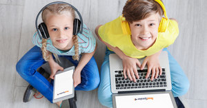 Two children are using computers while smiling.